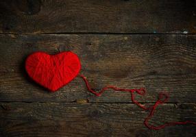 Red heart shape made from wool on old shabby wooden background photo