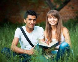 Two students studying in park on grass with book outdoors photo