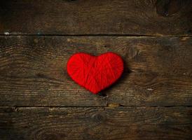 Red heart shape made from wool on old shabby wooden background photo