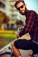 Young man in sunglasses riding a bike on city street photo