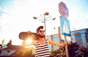 Stylish man in sunglasses with a skateboard on a street in the city at sunset light photo