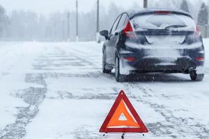 Closeup of red warning triangle with a broken down car in winter photo