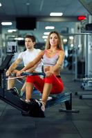 Athletic man and woman doing workout on rowing simulator in crossfit gym photo