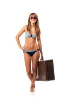 Full length portrait of a beautiful young woman posing in a bikini and sunglasses with a suitcase in hand on white photo