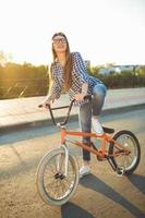 Lovely young woman in a hat riding a bicycle on city background in the sunlight outdoor photo