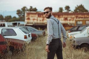 joven hermoso elegante hombre, vistiendo camisa y corbata de moño en el campo de antiguo carros foto