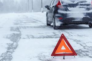 Closeup of red warning triangle with a broken down car in winter photo