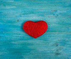 Red heart shape made from wool on blue wooden background photo