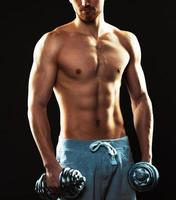 Athletic man with dumbbells on the black photo