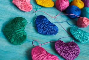 Multicolored Hearts with a balls of thread on blue wooden background photo