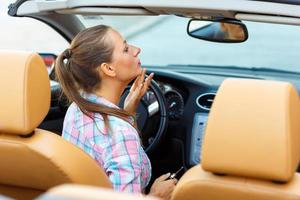 Woman corrects makeup looking in the rearview mirror in a convertible photo