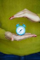 Little blue alarm clock in the hands of woman photo