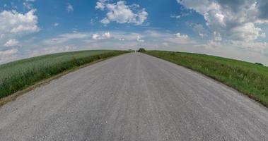 tiny planet transformation with curvature of space among fields on gravel road in sunny day with sky and fluffy clouds video