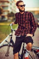 elegante hombre en Gafas de sol montando un bicicleta en ciudad calle foto