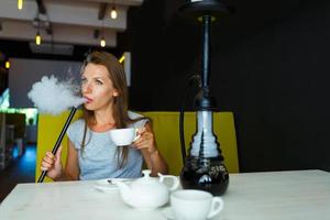 Beautiful woman smoking a hookah and drinking tea in a cafe photo