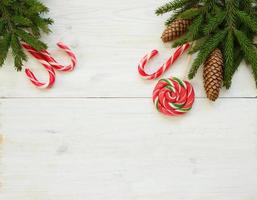 Christmas border with fir tree branches with cones and candy cane on white wooden boards photo
