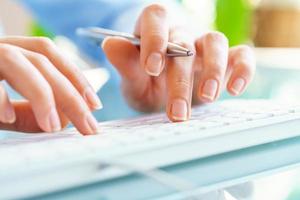 Woman office worker with pen in hand typing on the keyboard photo