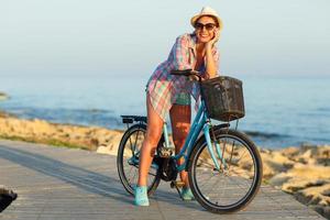 despreocupado mujer con bicicleta montando en un de madera camino a el mar, teniendo divertido y sonriente foto