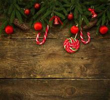 Borde de Navidad con ramas de abeto, conos, adornos navideños y bastón de caramelo sobre tablas de madera rústica foto