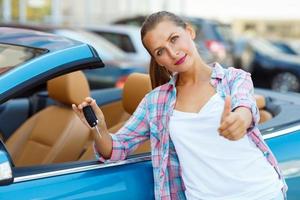 joven contento mujer en pie cerca un convertible con el llaves en su mano y pulgar arriba foto