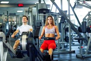 atlético hombre y mujer haciendo rutina de ejercicio en remo simulador en crossfit gimnasio foto