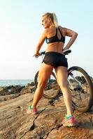 Happy athletic woman standing on the rocks with a bicycle and enjoy the view photo