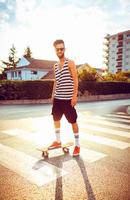 Stylish man in sunglasses with a skateboard on a street in the city at sunset light photo