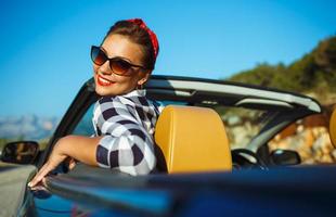 hermosa alfiler arriba mujer sentado en cabriolé, disfrutando viaje en lujo moderno coche con abierto techo foto