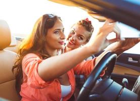 dos joven hermosa muchachas son haciendo selfie en un convertible foto