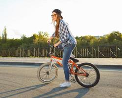encantador joven mujer en un sombrero montando un bicicleta en ciudad antecedentes en el luz de sol al aire libre foto