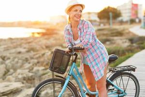 despreocupado mujer con bicicleta montando en un de madera camino a el mar, teniendo divertido y sonriente foto