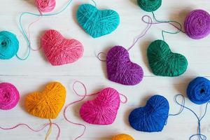 Multicolored Hearts with a balls of thread on white wooden background photo