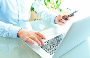 Men office worker typing on the keyboard and using smartphone photo