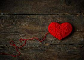 Red heart shape made from wool on old shabby wooden background photo