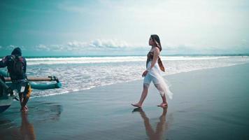 un asiatico donna nel un' bianca vestito a piedi solo su il spiaggia con un' triste espressione e il mare onde dietro a sua video