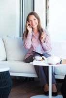 Smiling businesswoman talking on the cellphone and writing in organizer in a coffee house photo