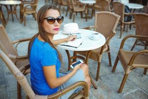 Candid image of a young woman using smartphone and makes notes in a notebook in a cafe photo
