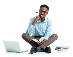 Happy african american college student with laptop, books and bottle of water sitting on white photo