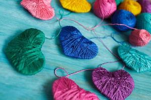 Multicolored Hearts with a balls of thread on blue wooden background photo