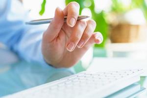 Woman office worker with pen in hand typing on the keyboard photo