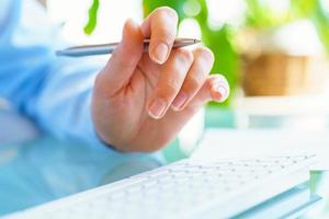 Woman office worker with pen in hand typing on the keyboard photo