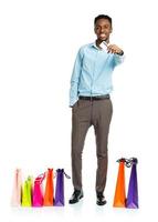 contento africano americano hombre con compras pantalones y participación crédito tarjeta en blanco antecedentes. Días festivos concepto foto