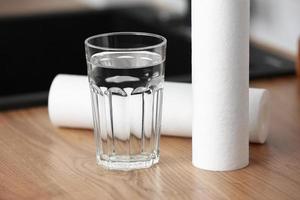 A glass of clean water and foamed polypropylene filter cartridges on wooden table in a kitchen interior. Installation of reverse osmosis water purification system. Concept Household filtration system. photo