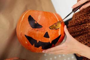 Close up of young woman carving Jack O Lattern from ripe orange pumpkin with knife on her wooden kitchen table. Female preparing all hallows eve Halloween party decorations. Background, copy space. photo