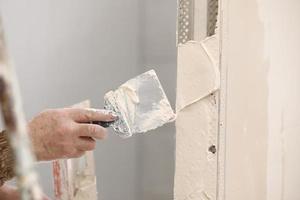 Builder using a trowel to add plaster. Plastering wall with putty-knife, close up image. Fixing wall surface and preparation for painting. construction work during quarantine photo