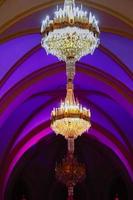 Elegant luxury crystal chandeliers on ceiling in purple and blue light. Emphasis on luxury, used in various places such as palace church, residence. Decorative elegant vintage and Contemporary Concept photo