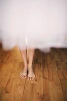 piernas de el novia son ocultación para un Boda vestido. piernas de el niña en el de madera piso foto