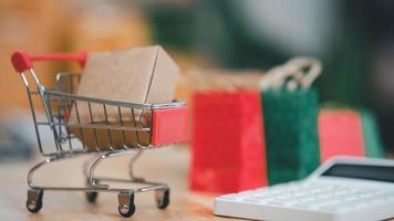 Shopping cart, cardboard box and calculator on the table ,Consumer society ,Shopping service on online web and offers home delivery ,online shopping or e-shopping photo
