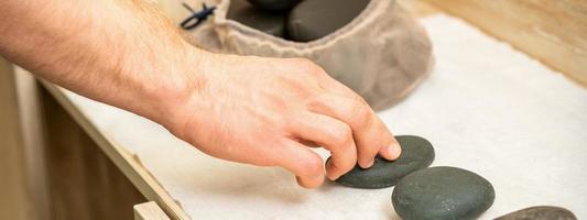 Masseur takes black massage stones photo