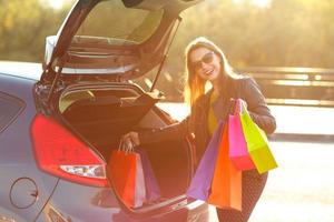 Smiling Caucasian woman putting her shopping bags into the car trunk photo